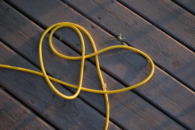 A yellow garden hose loosely coiled on a wooden deck