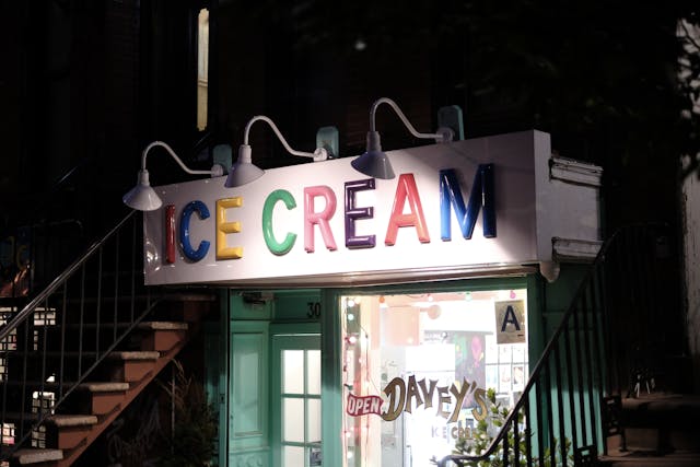 A brightly lit ice cream shop with a colorful sign reading ICE CREAM in large letters, located between two staircases