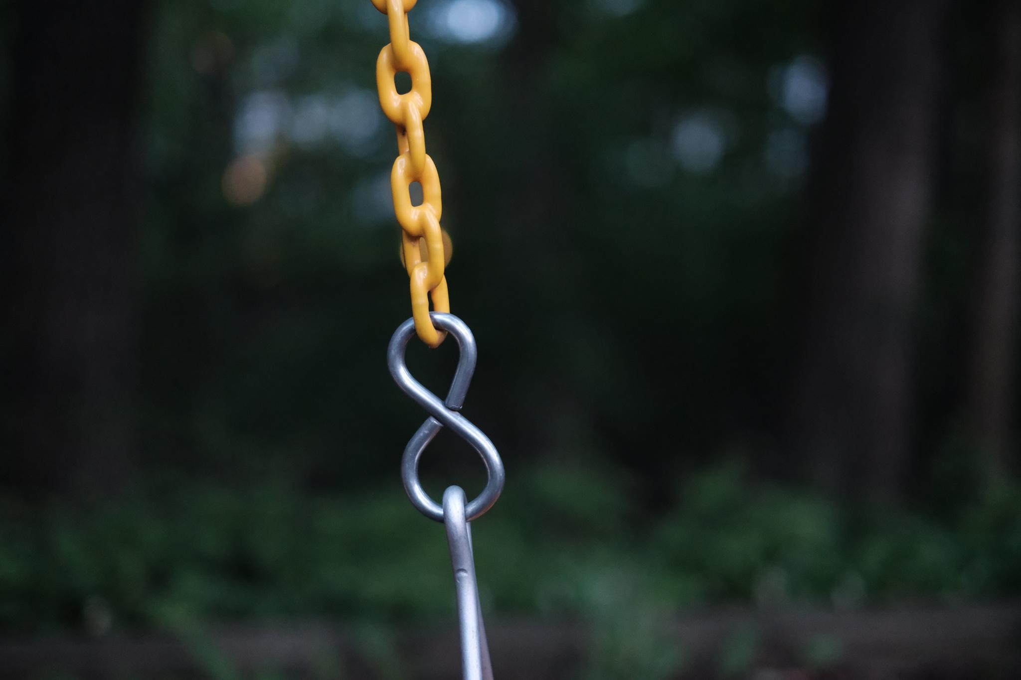 A yellow chain linked to a metal hook against a blurred natural background