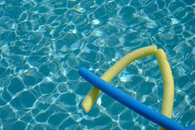 A swimming pool with two pool noodles, one yellow and one blue, floating on the water