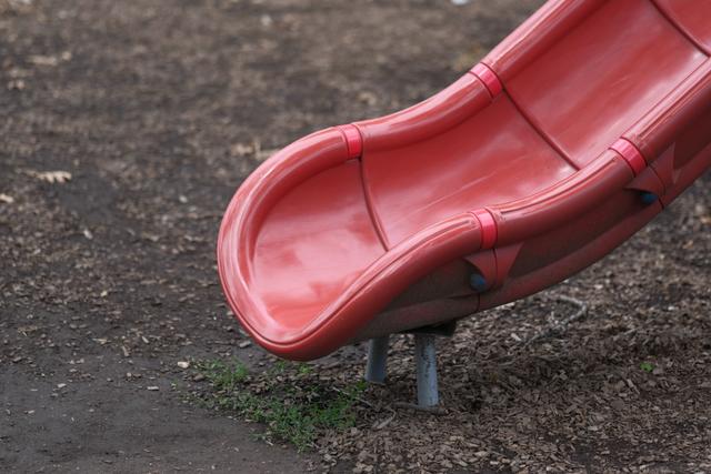 A red playground slide ending on a dirt and mulch surface
