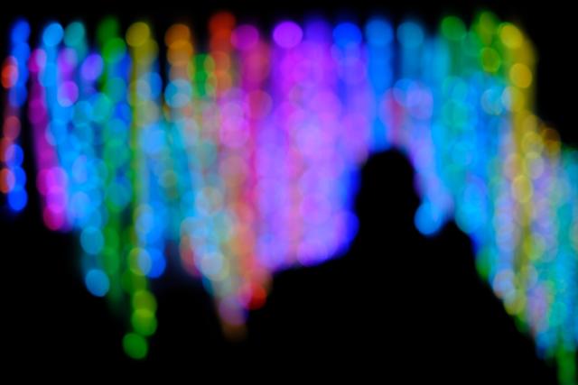 A blurred silhouette of a person in front of a vibrant, multicolored light display