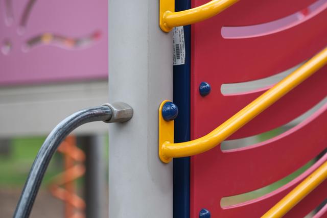 A close-up of colorful playground equipment featuring yellow bars, a pink panel with curved cutouts, and a metal handrail