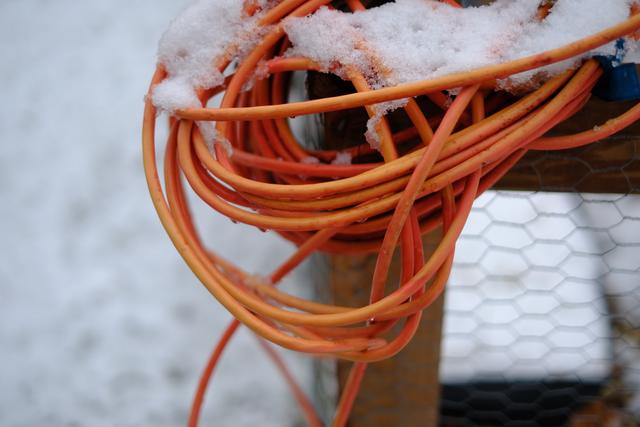 A bundle of orange extension cords covered in snow, draped over a wooden structure with a wire mesh