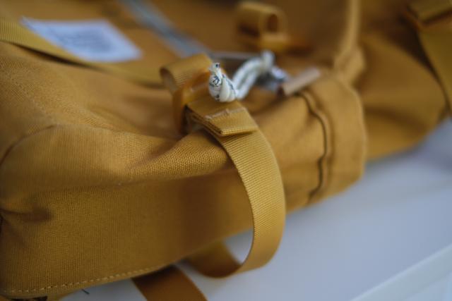 A close-up of a mustard yellow backpack with a focus on the strap and buckle