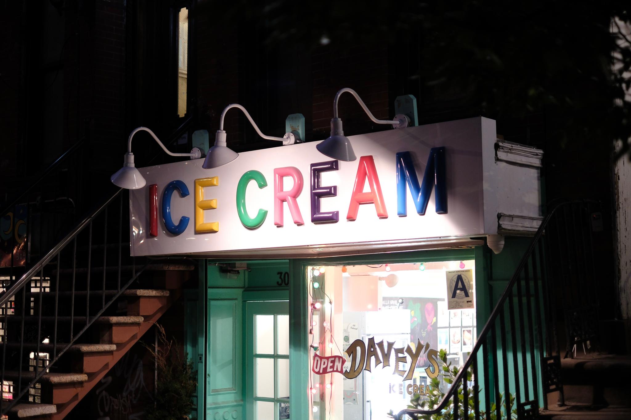 A brightly lit ice cream shop with a colorful sign reading ICE CREAM in large letters, located between two staircases