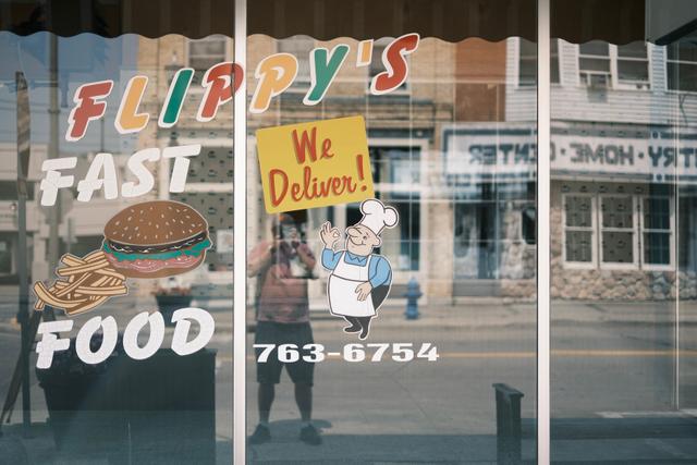 A storefront window with the text FLIPPY'S FAST FOOD and a cartoon chef holding a sign that says We Deliver! along with a phone number. The window also features images of a burger and fries