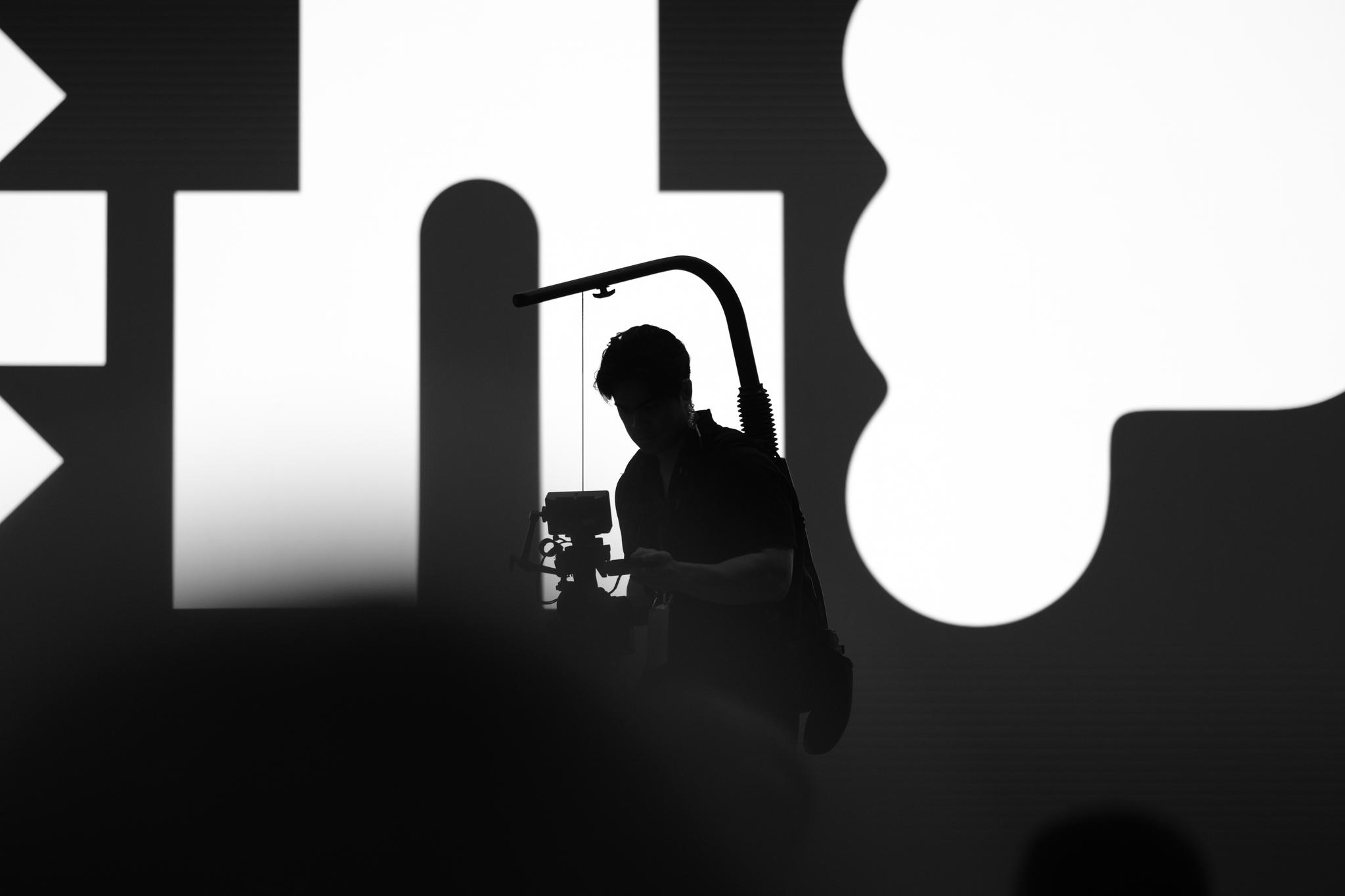 A silhouette of a person operating a camera against a backdrop of abstract black and white shapes