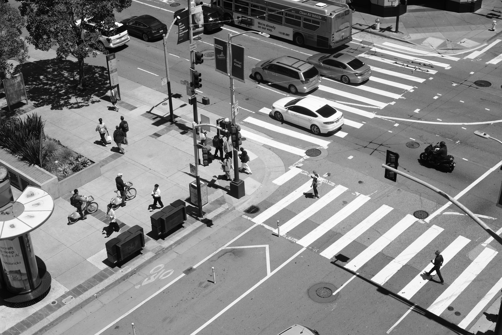 A busy urban intersection with pedestrians crossing the street and vehicles, including a bus, navigating the roads