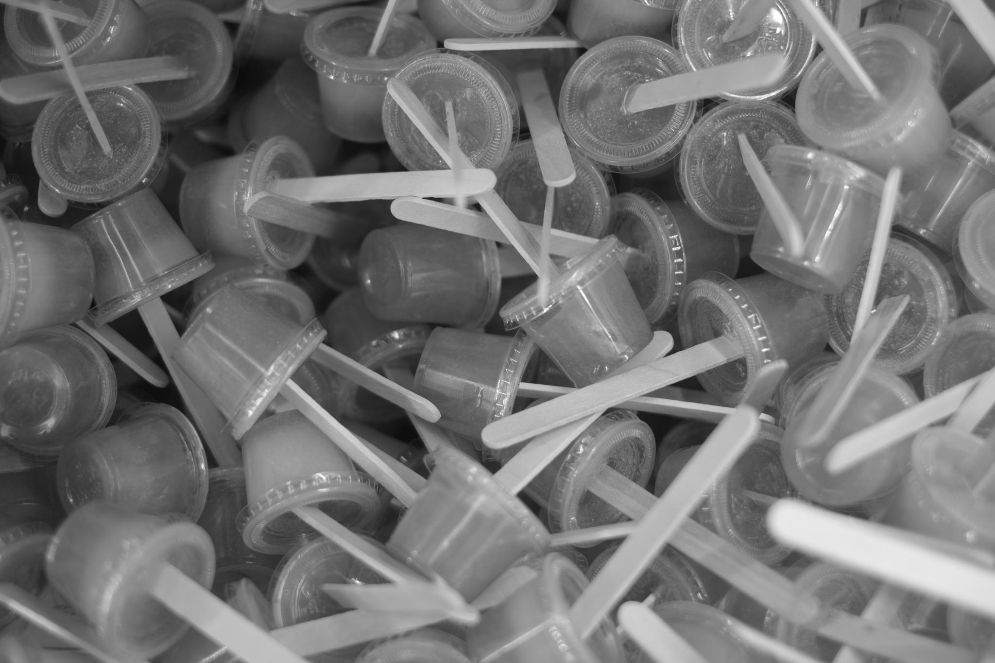 A pile of small plastic containers with attached lids and stirrers, all in grayscale