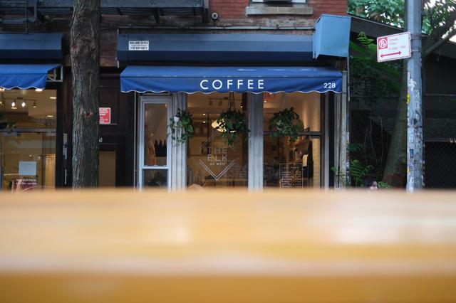 A coffee shop with a blue awning and the word COFFEE written on it, viewed from behind a blurred foreground