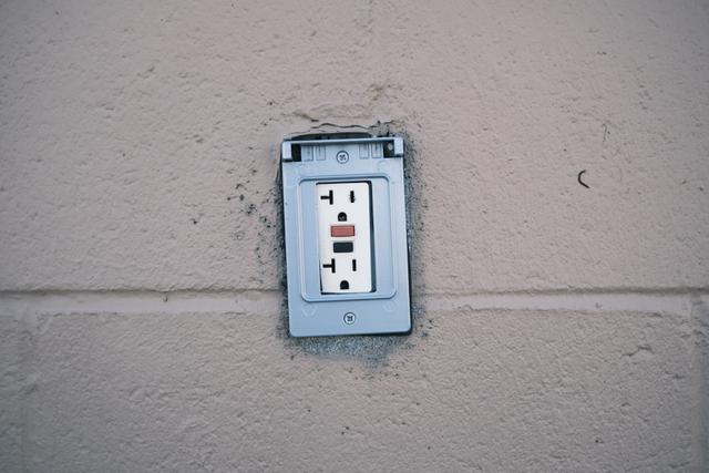 A wall-mounted electrical outlet with a protective cover, set against a beige concrete wall