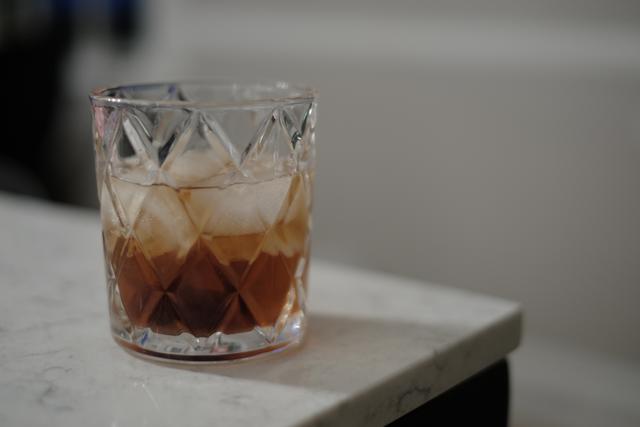 A glass filled with a brown liquid and ice cubes, placed on a marble surface