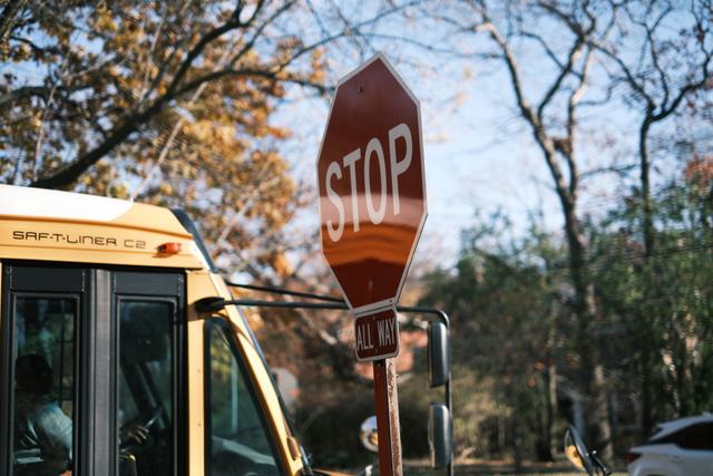 A stop sign next to a school bus with trees and a clear sky in the background