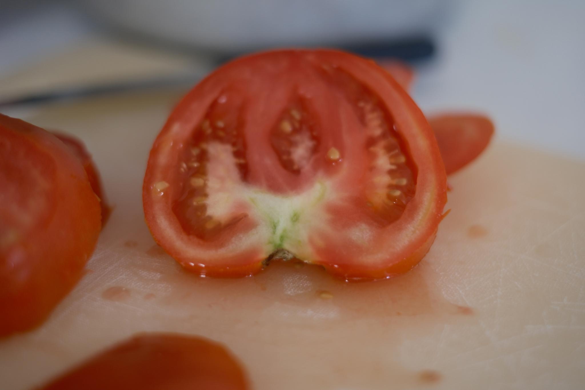 A halved tomato on a cutting board, with visible seeds and internal structure