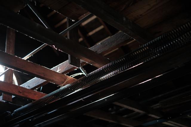 Exposed wooden beams and metal pipes in a dimly lit ceiling space