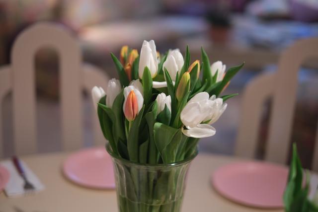 A bouquet of white and pink tulips in a glass vase on a table set with pink plates