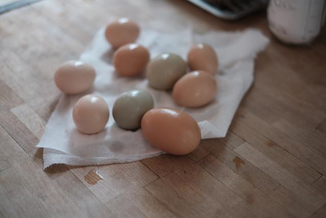 Several eggs with varying shell colors are resting on a paper towel on a wooden surface, with a blurred background suggesting a kitchen setting