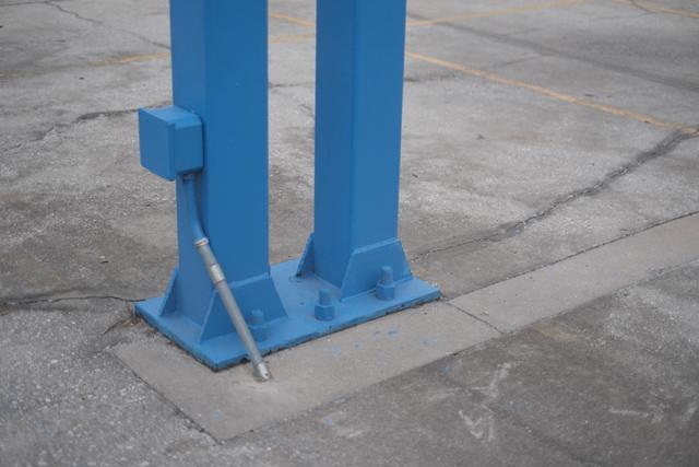 Two blue metal columns anchored to a concrete surface, with a cable connected to one of the columns