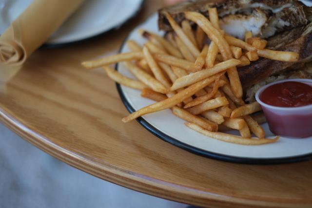 A plate of French fries with a side of ketchup on a wooden table, accompanied by a rolled napkin and an empty plate in the background