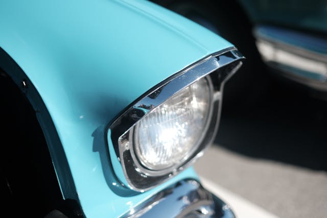 A close-up of a turquoise vintage car's headlight with chrome trim