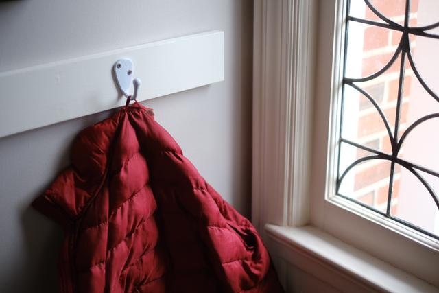 A red puffer jacket hanging on a white hook next to a window with decorative ironwork