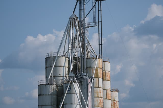 Several large, cylindrical metal silos with a network of pipes and ladders against a backdrop of a partly cloudy sky