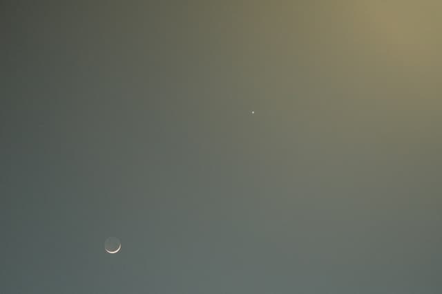 A crescent moon and a small bright dot against a gradient sky transitioning from blue to yellow