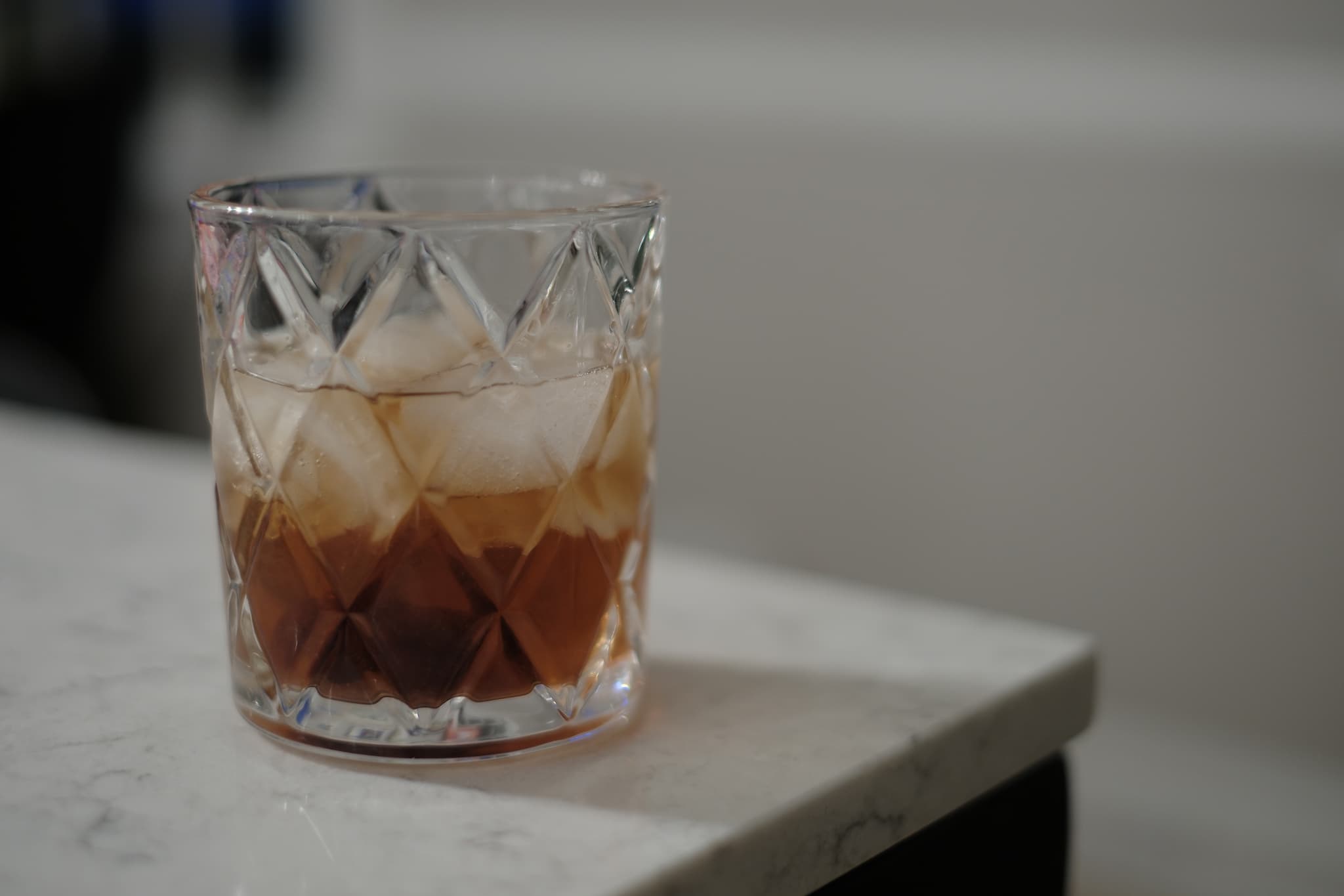 A glass filled with a brown liquid and ice cubes, placed on a marble surface