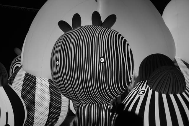 Black-and-white illustration of zebra heads in close-up, with bold striped patterns and cartoon-style eyes overlapping against a light circular backdrop