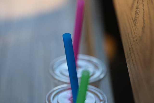 Two cups with colorful straws on a wooden surface, featuring blurred background and soft lighting