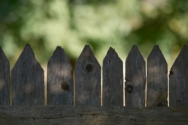 A wooden picket fence with a blurred green background