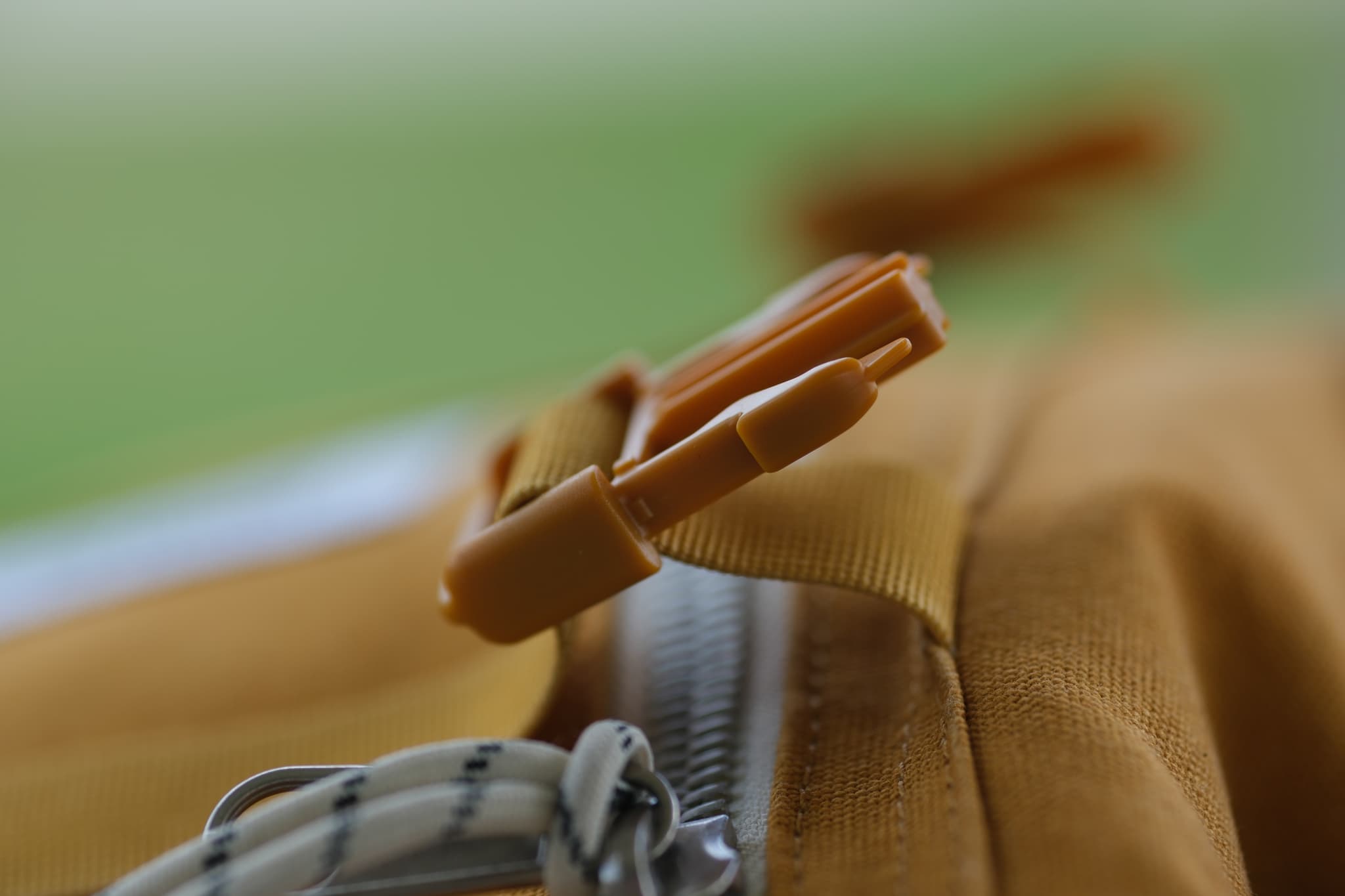 A close-up of a backpack zipper on a brown fabric, with a green blurred background