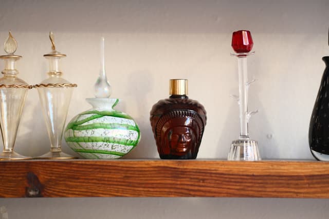 Row of decorative glass bottles and a green-striped vase on a wooden shelf against a light wall