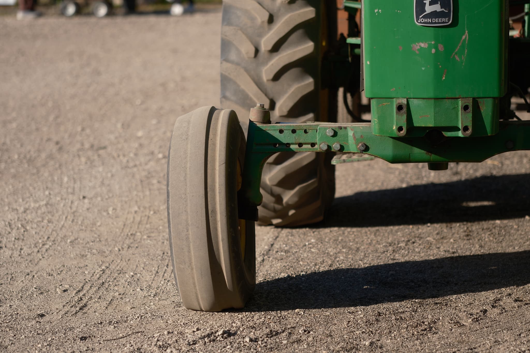 A close-up of a green tractor's front wheel on a dirt surface