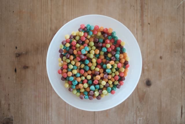 A white bowl filled with colorful, round cereal pieces on a wooden surface