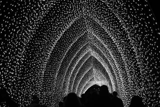 A tunnel illuminated by countless small lights, creating an arching, cathedral-like effect with silhouetted figures walking through