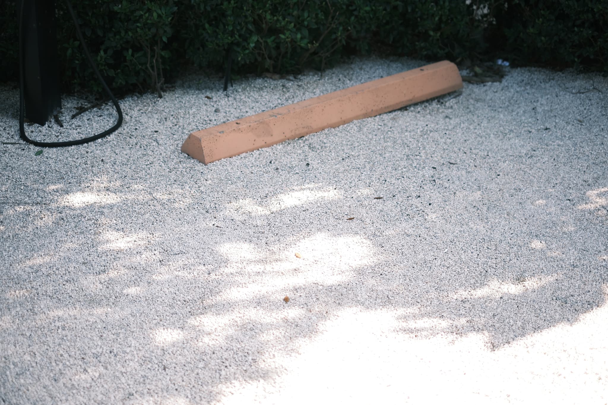 A gravel surface with a single orange parking block near some greenery