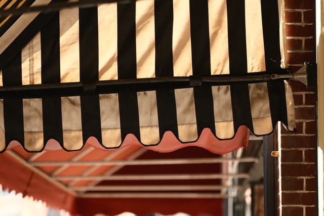 Close-up of striped awnings on brick storefronts, with a black-and-white canopy in the foreground and a red-and-white canopy behind