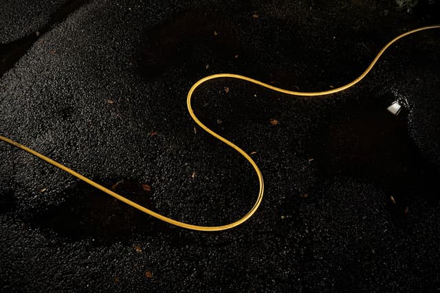 A thin yellow cord winds in graceful curves across a dark, grainy surface