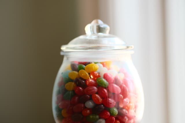 A glass jar filled with colorful jelly beans, topped with a clear lid, against a softly lit background