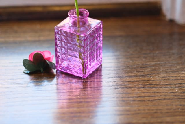 Small pink translucent cube gift with ribbon on a wooden floor, with a tiny decorative figure beside it