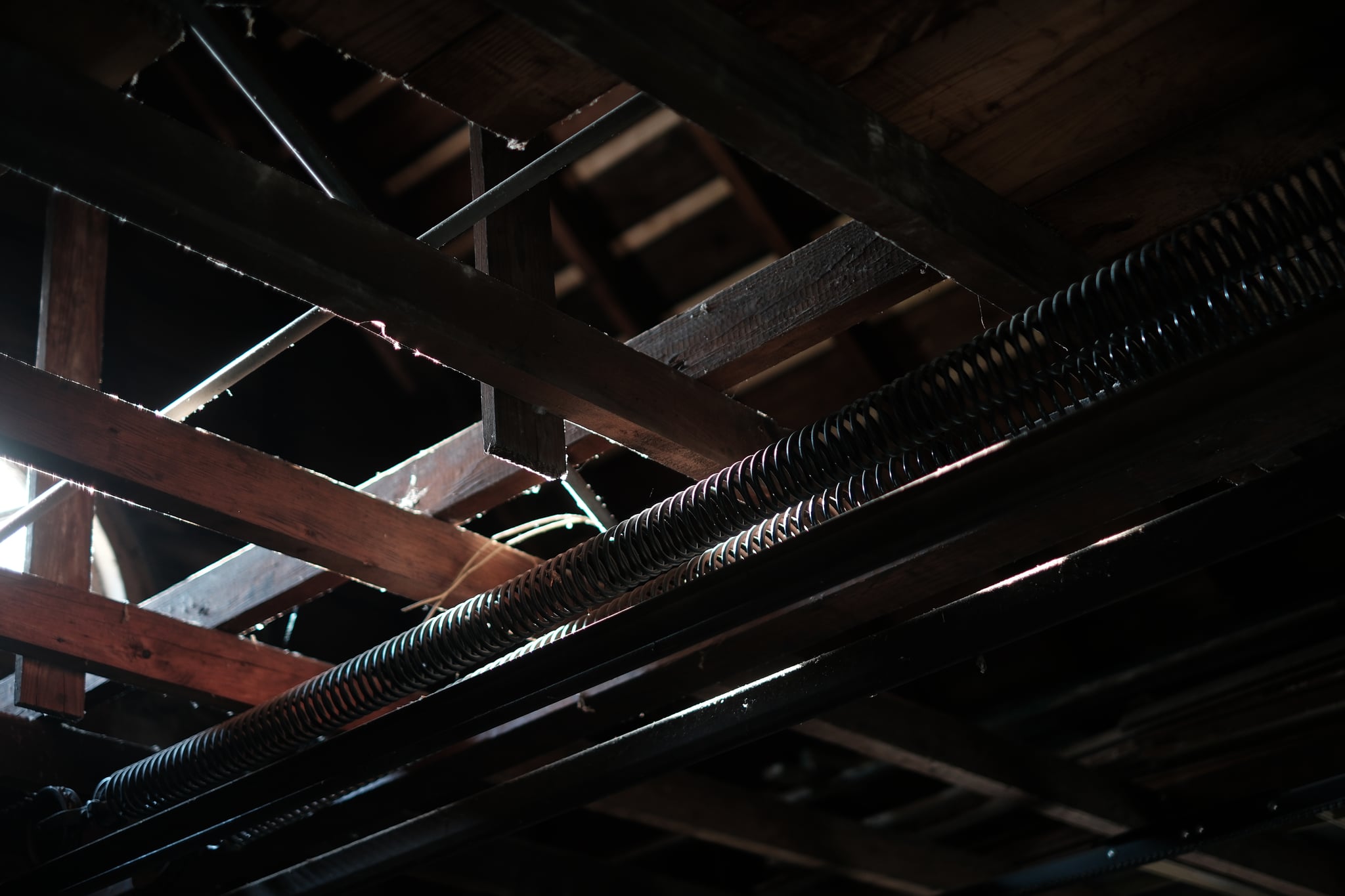 Exposed wooden beams and metal pipes in a dimly lit ceiling space