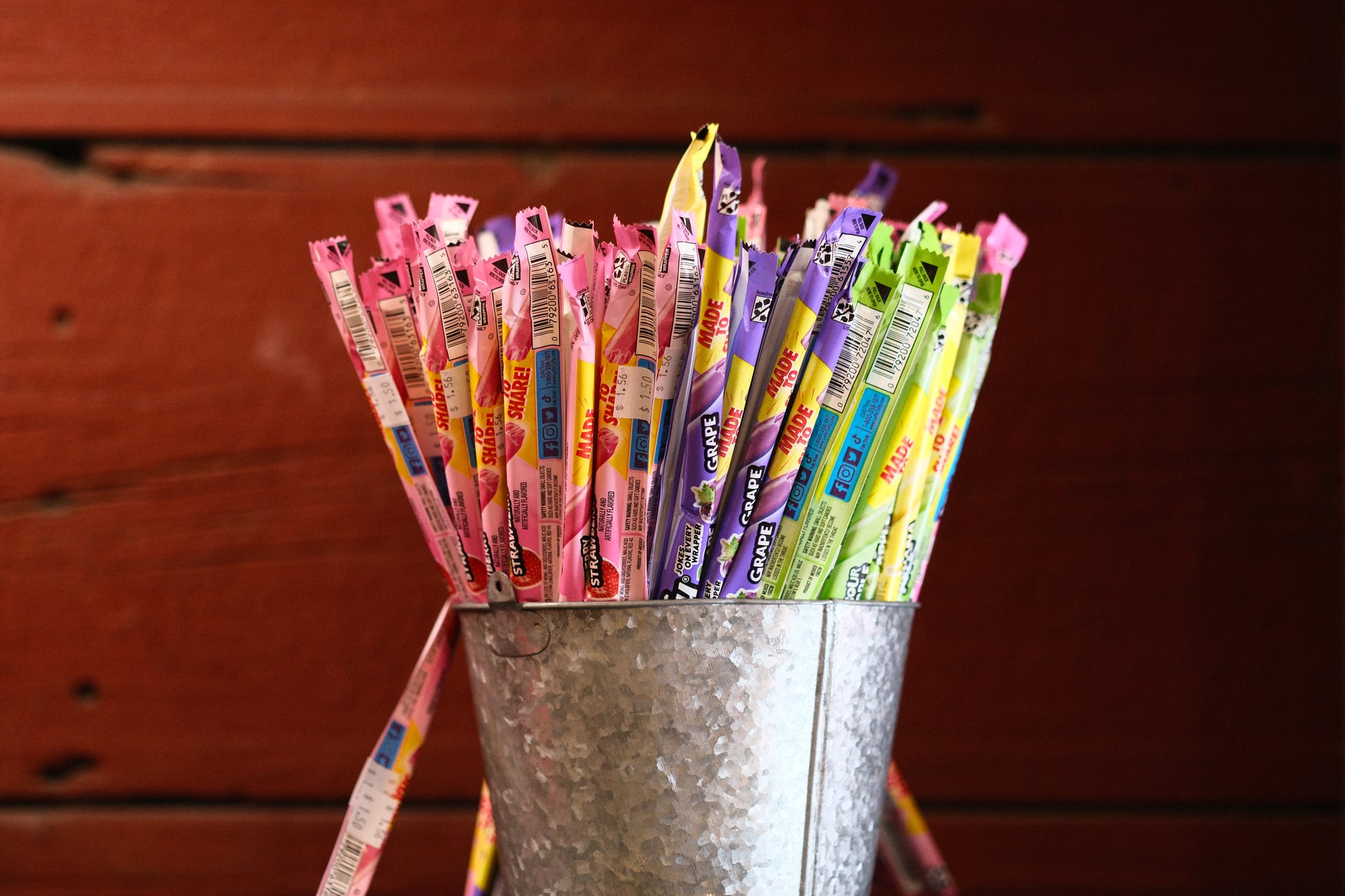Glass jar filled with colorful patterned drinking straws on a wooden table, with two straws leaning against the jar