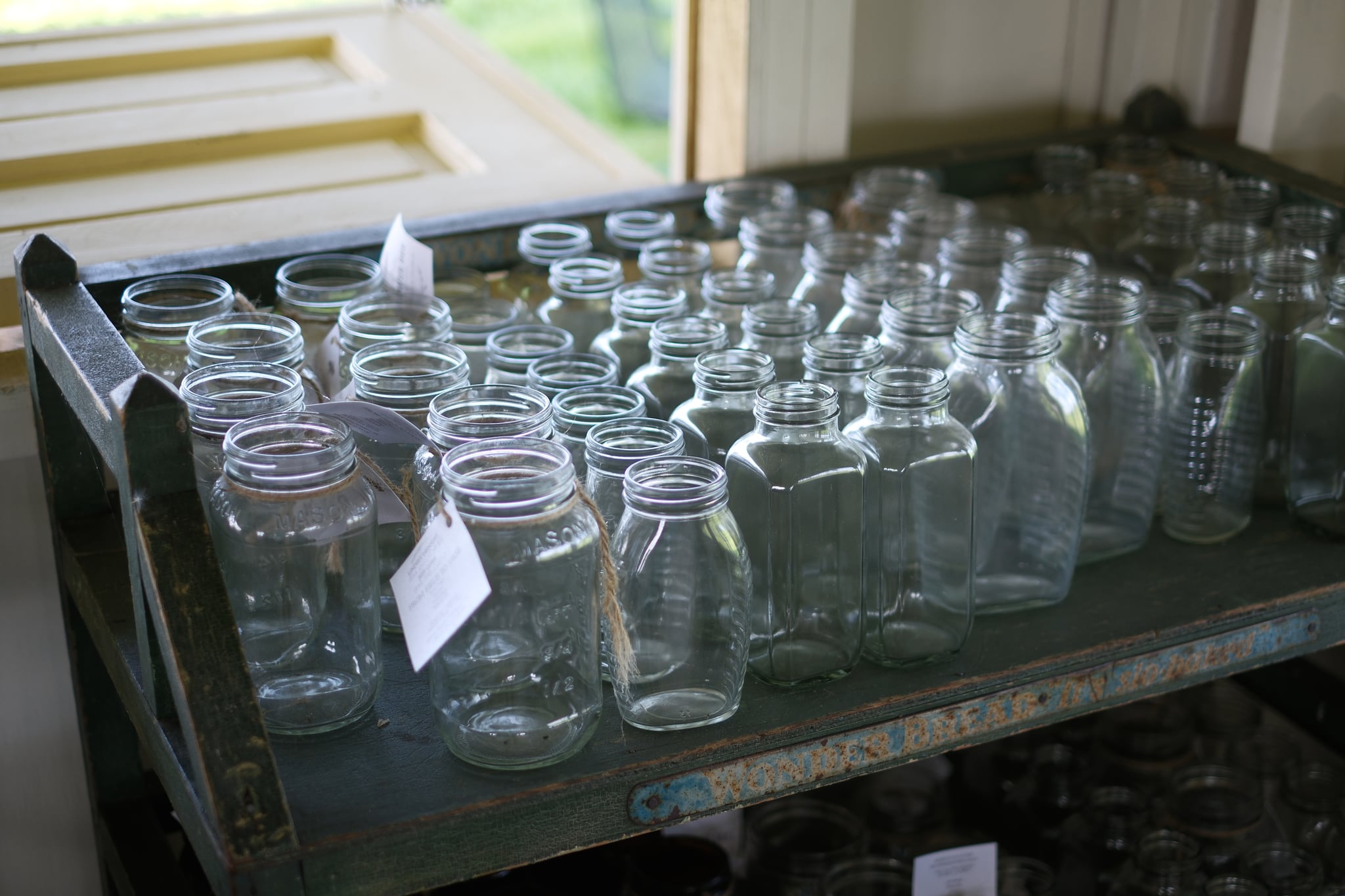 A collection of empty glass jars arranged on a metal shelf near a window