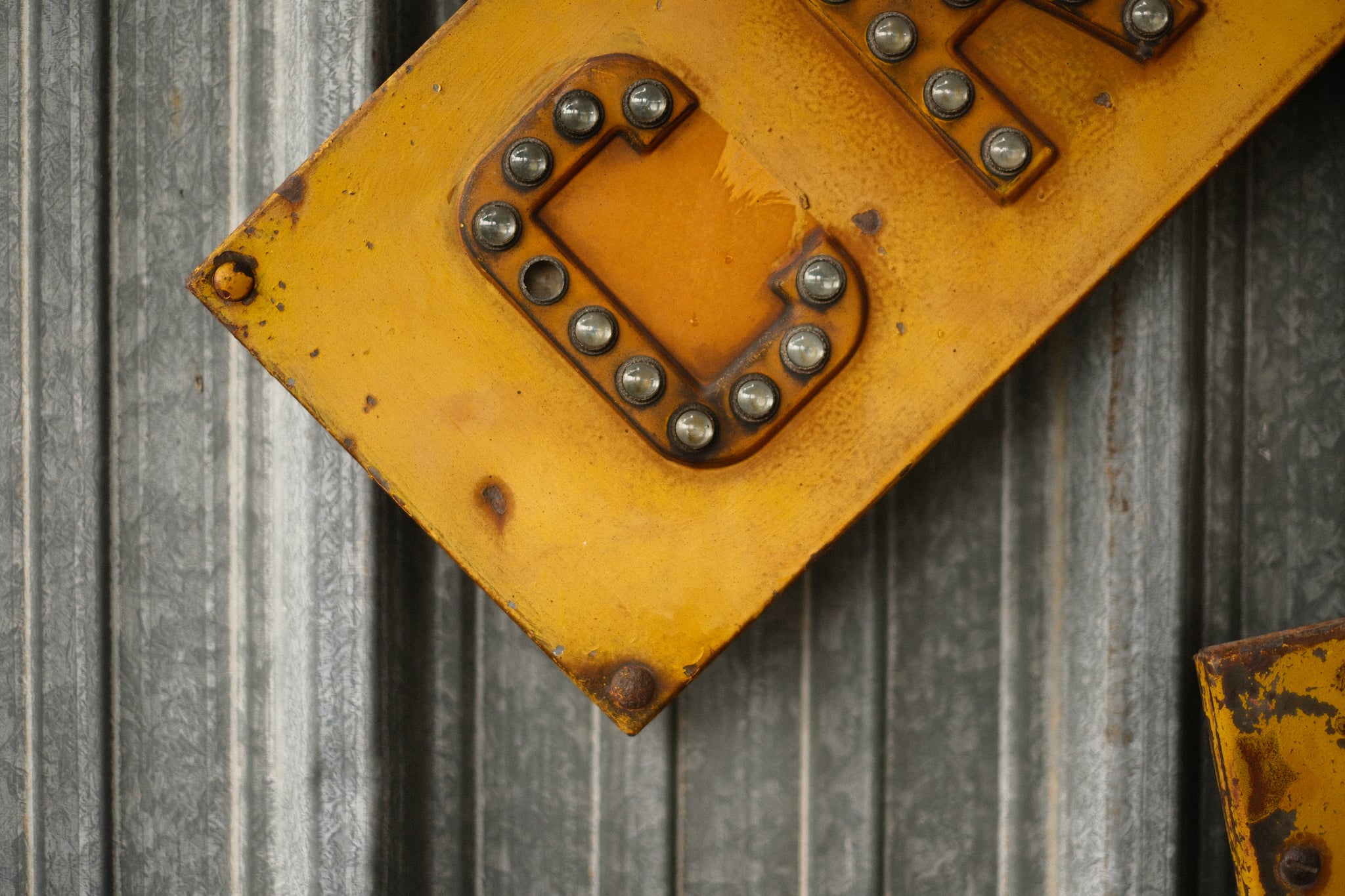 Yellow riveted metal plate with a raised letter C lying diagonally on weathered gray wooden planks