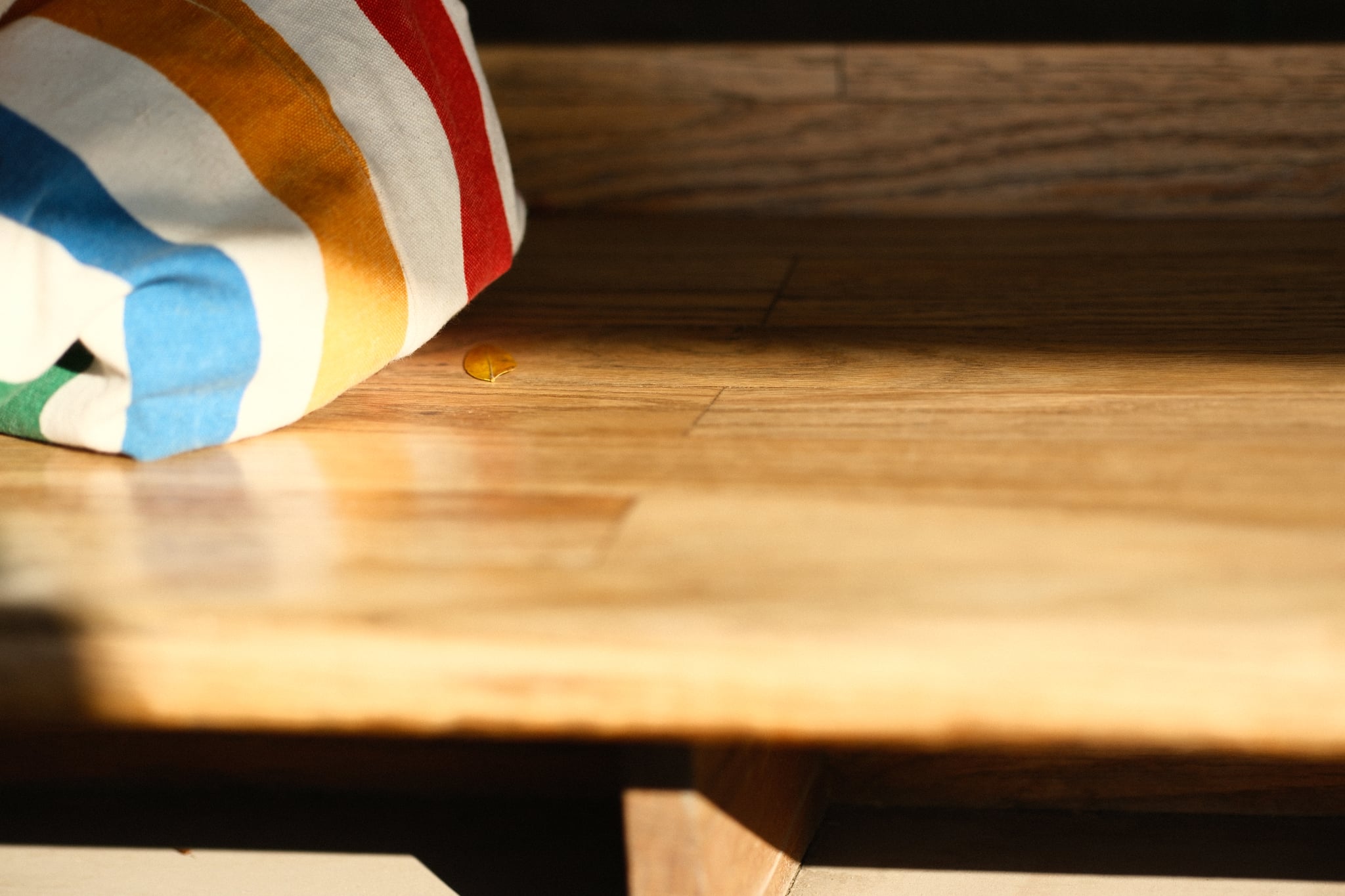 A wooden surface bathed in warm sunlight with a colorful striped fabric in the corner