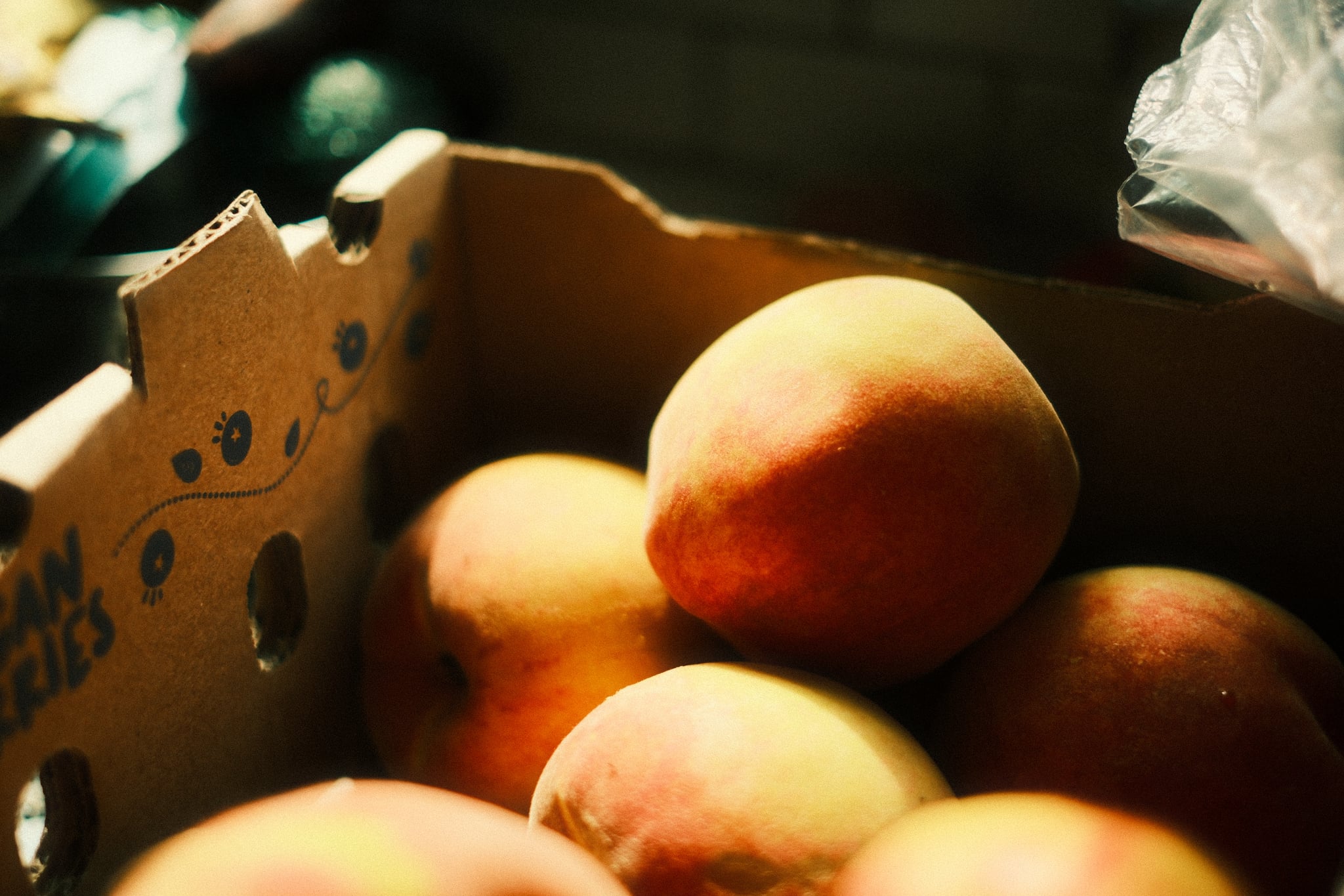 Ripe peaches piled in a cardboard produce crate under warm light