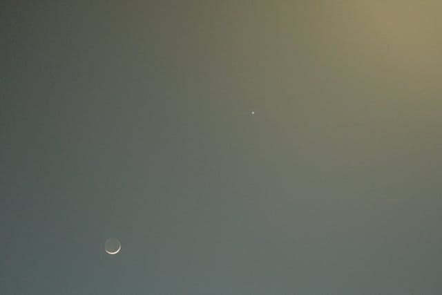A crescent moon and a small bright dot against a gradient sky transitioning from blue to yellow