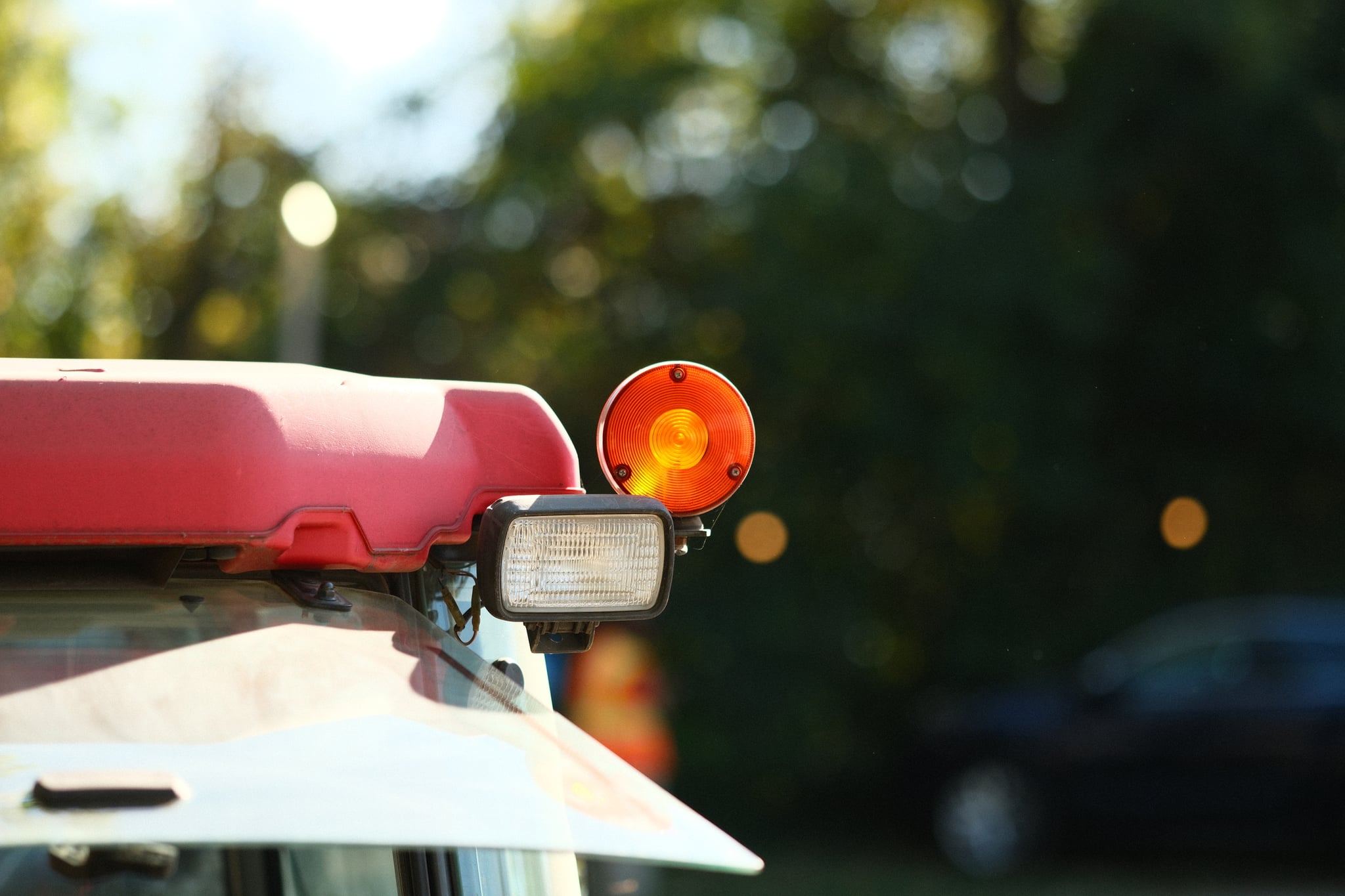 Close-up of a vehicle's orange warning light against a blurred background of trees and greenery